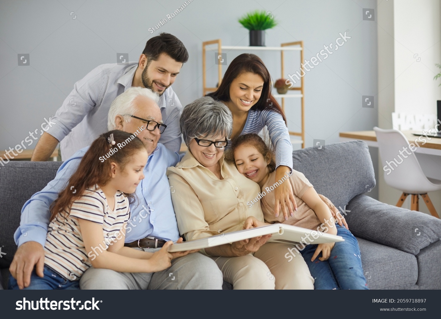 Happy big family grandparents with twin granddaughters and their parents browse the family photo album and share happy memories. Family gathered together in the living room. Family connection concept. #2059718897