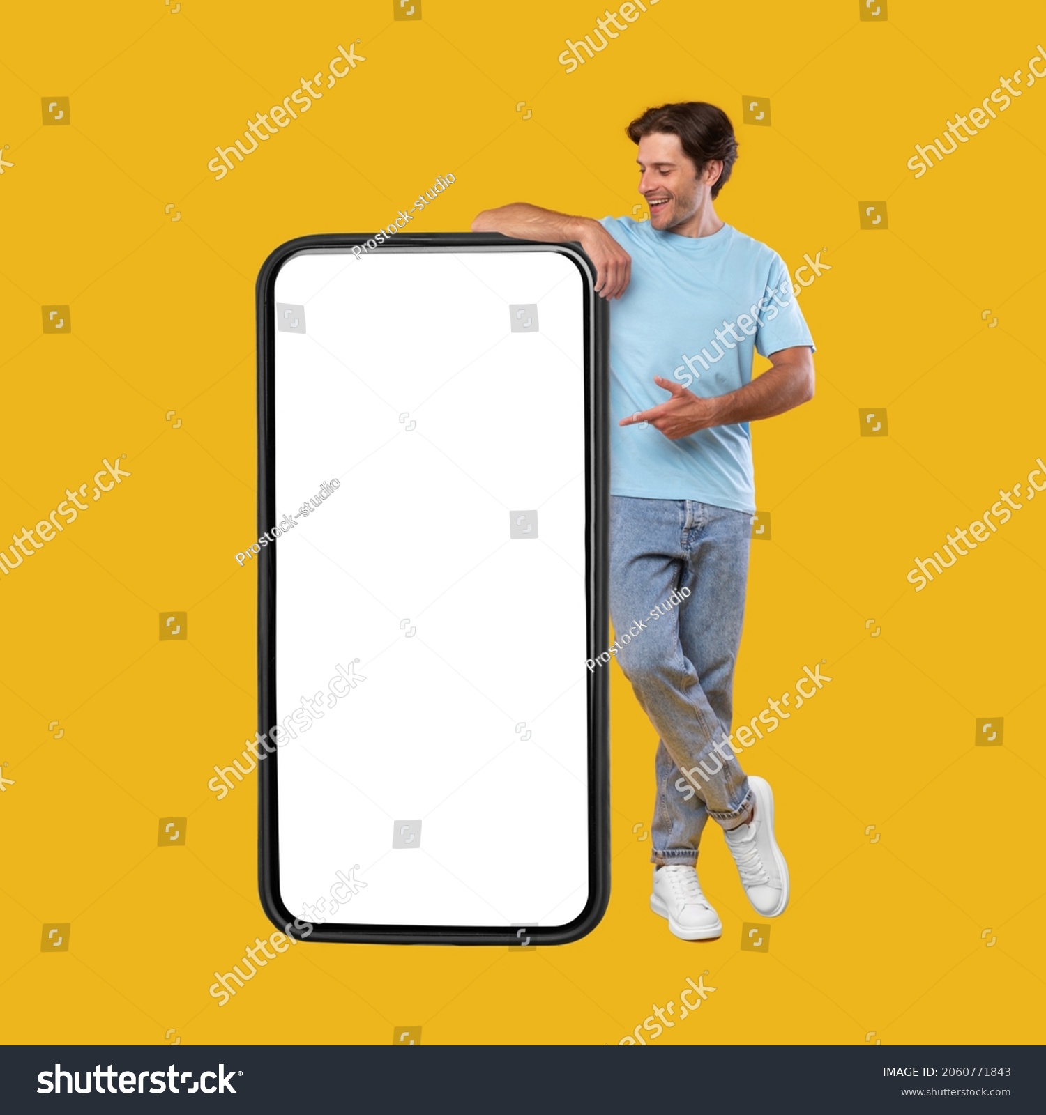 Mobile App Advertisement. Full Body Length Of Happy Man Leaning And Pointing At Big Huge White Empty Smartphone Screen Standing On Orange Studio Background. Check This Out, Cellphone Display Mock Up #2060771843