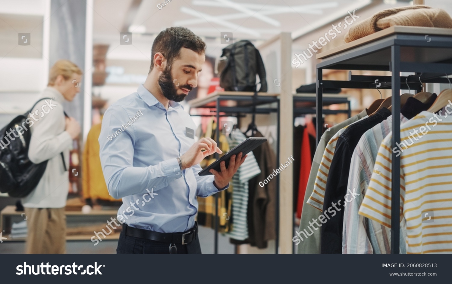 Clothing Store: Male Visual Merchandising Professional Uses Tablet Computer To Create Collection. Fashionable Shop Sales Retail Manager Checks Stock. Small Business Owner Orders Stylish Items #2060828513