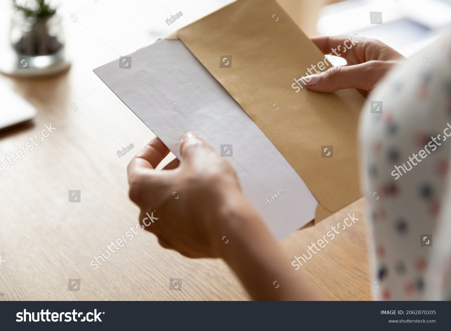 Hands of woman receiving letter, invitation, notification, postcard, taking out document for reading, opening envelope with blank folded paper at work desk. Mail concept. Close up, cropped shot #2062870205