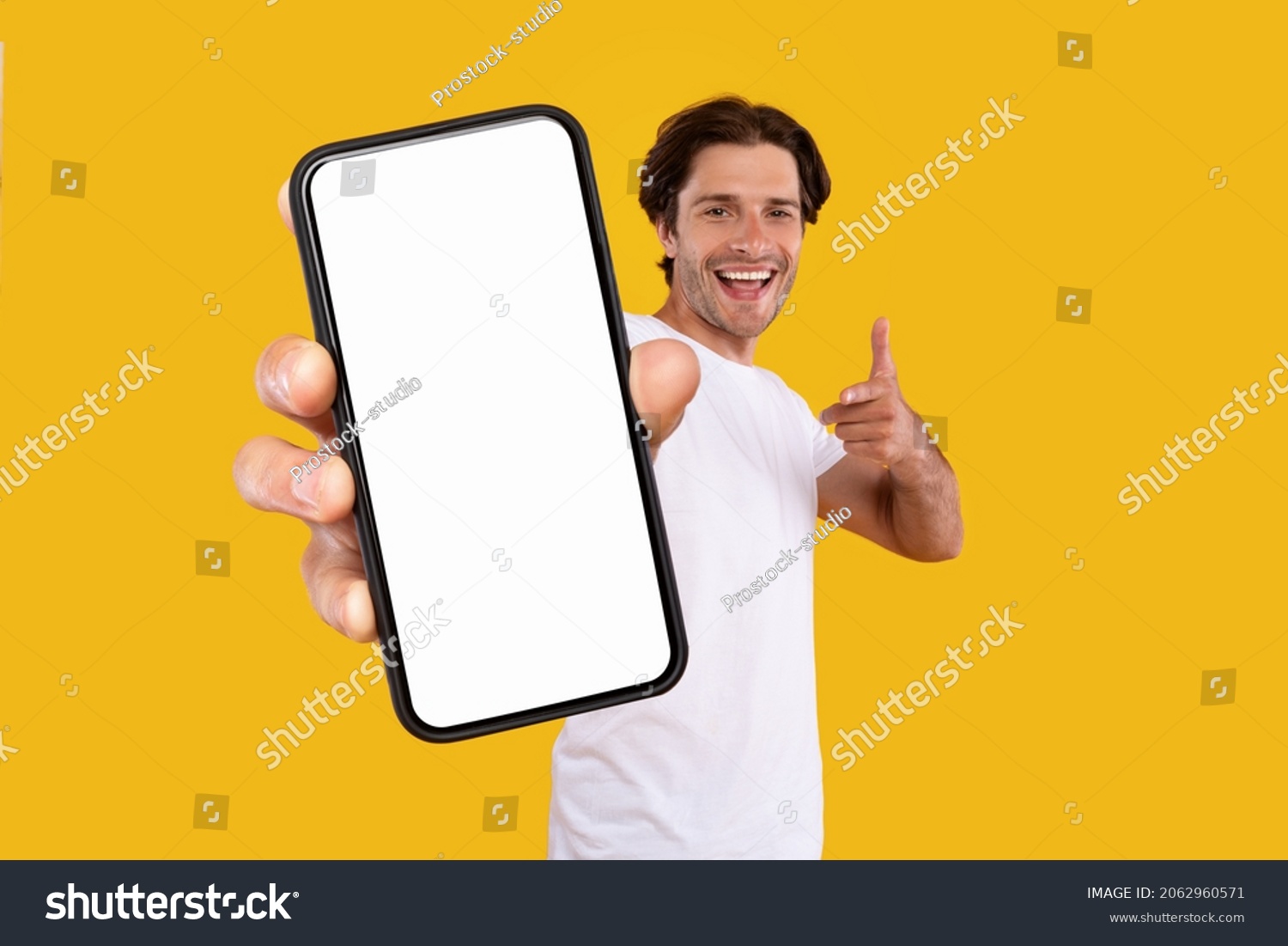 Mobile App Advertisement. Handsome Excited Man Showing Pointing At White Empty Smartphone Screen Posing Over Orange Studio Background, Smiling To Camera. Check This Out, Cellphone Display Mock Up #2062960571