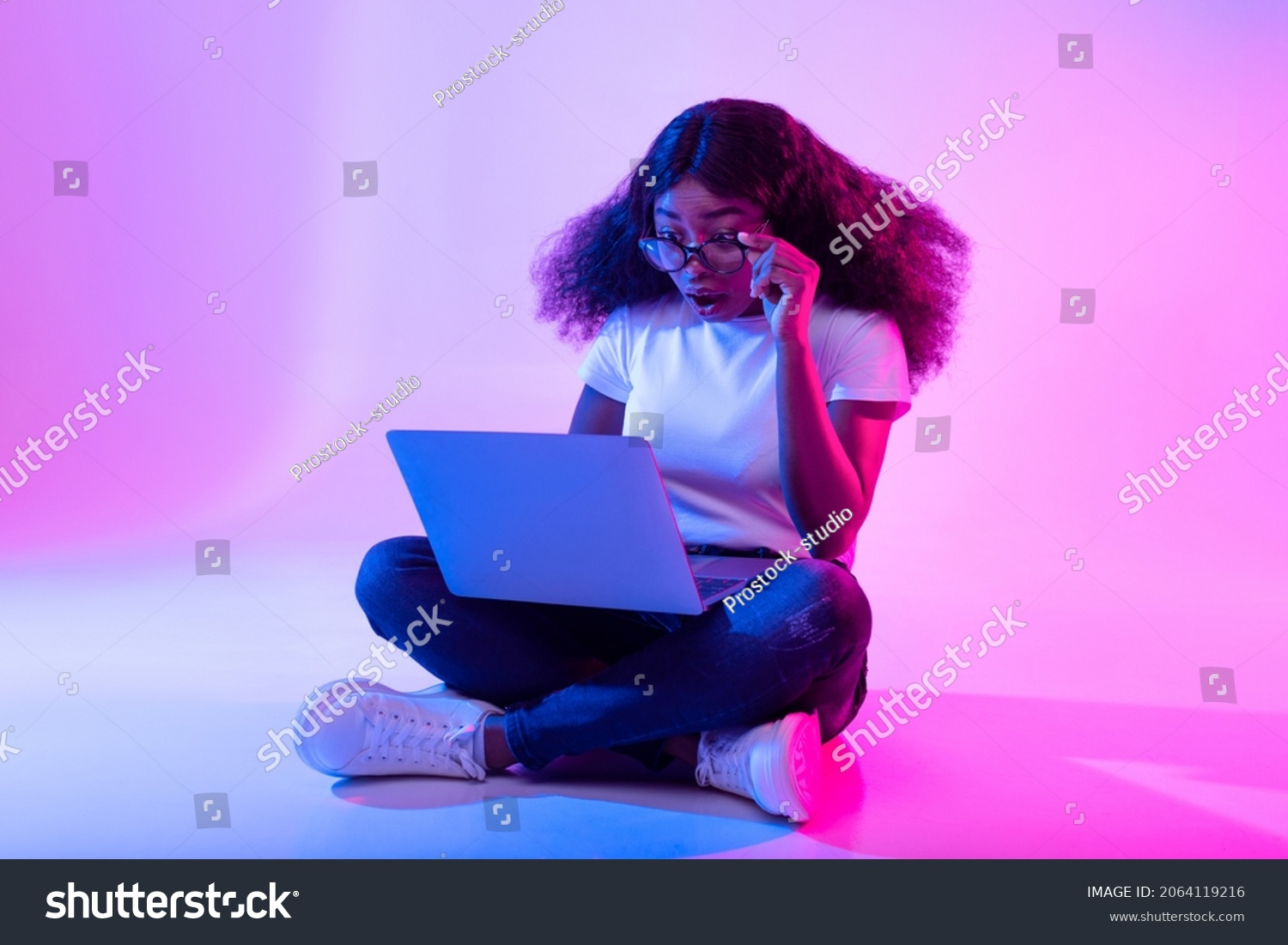 Deadline concept. Full length of surprised black woman using laptop computer, opening mouth in shock in neon light. Stressed African American lady working online, making error in project #2064119216