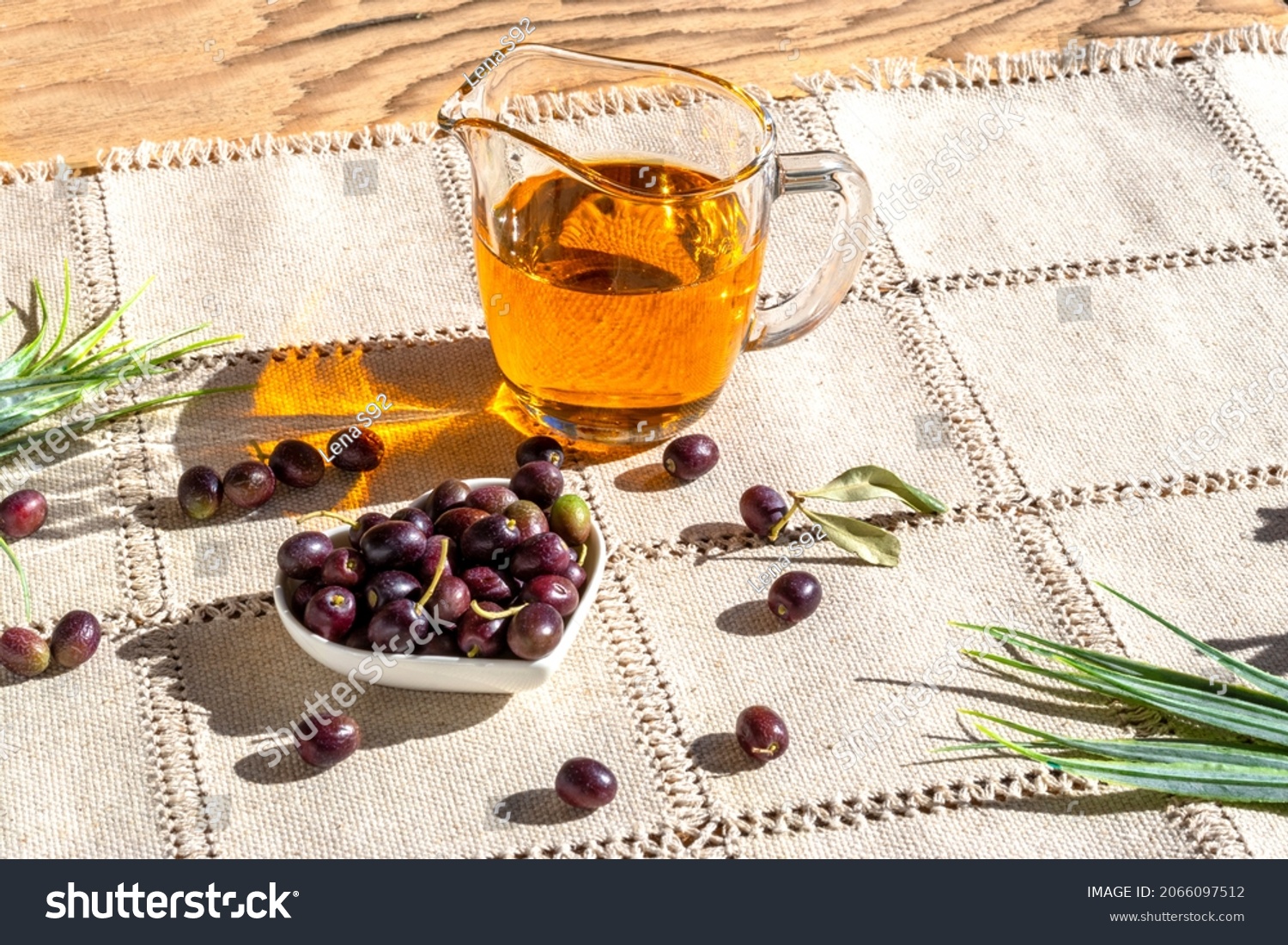 Freshly picked olive tree fruits and olive oil in glass saucepan. First cold pressed oil. Olea europaea. Napkin made of unpainted linen in rustic style #2066097512