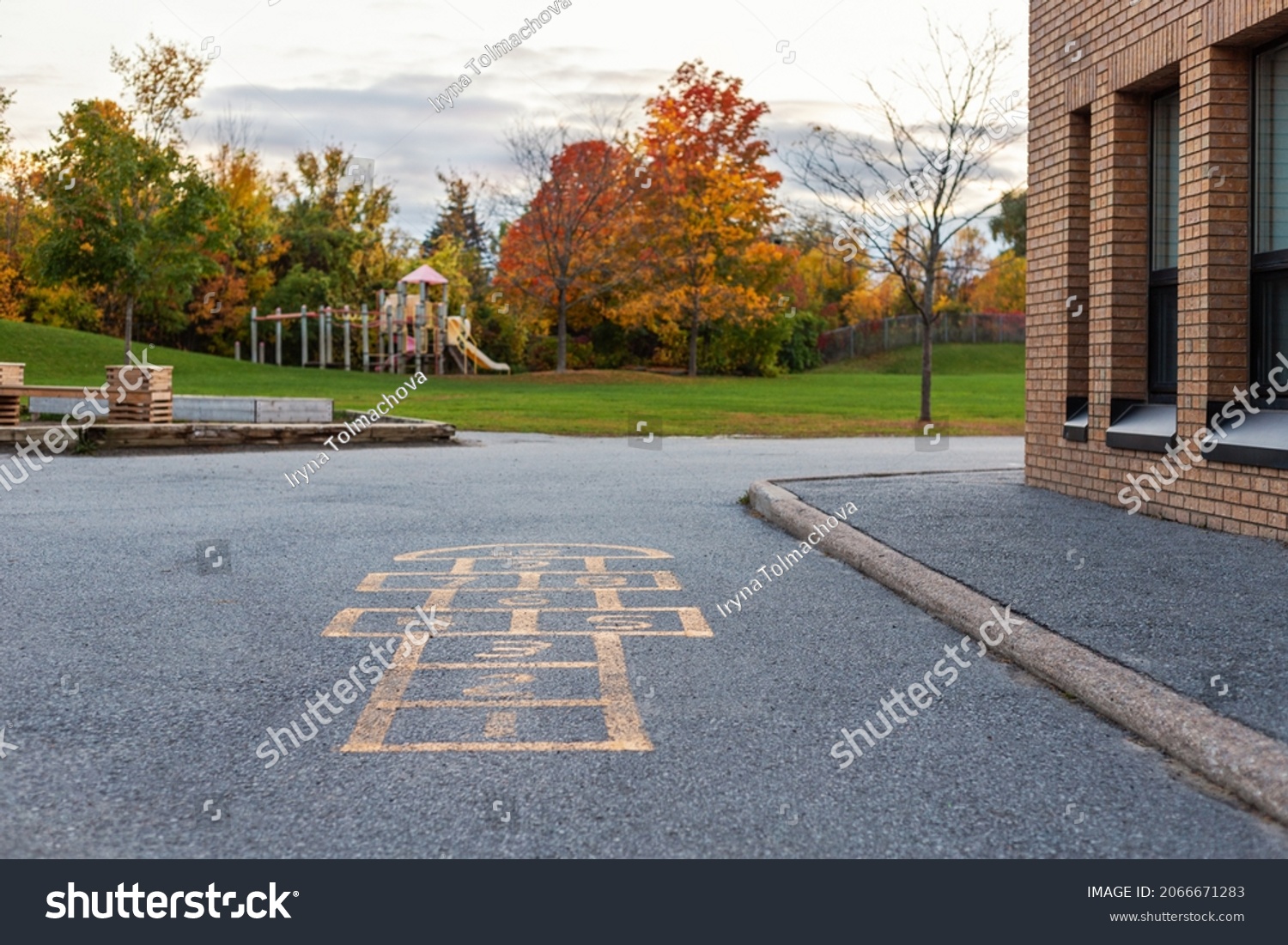 School building and schoolyard with playground for children in evening in fall season. Selective focus on hopscotch. Back to school educational concept #2066671283