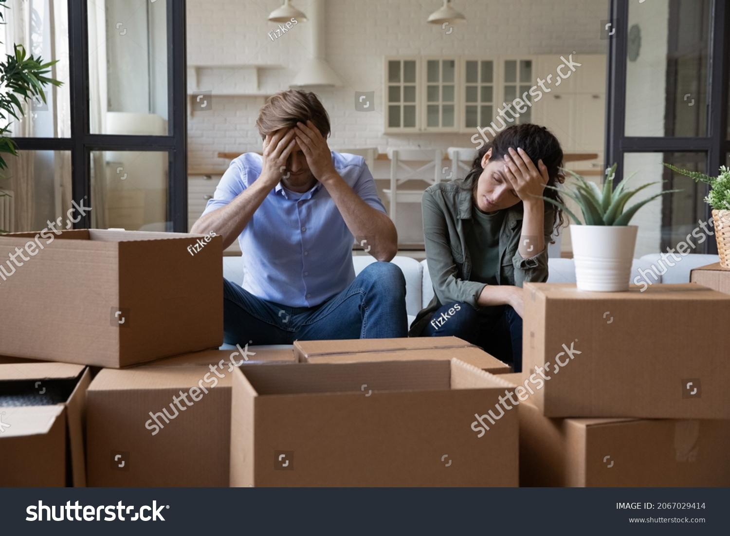 Exhausted young couple sit rest on sofa in living room near heap of cardboard boxes feel unmotivated to unpack their belongings. Financial problem, debt and eviction, hard long relocation day concept #2067029414