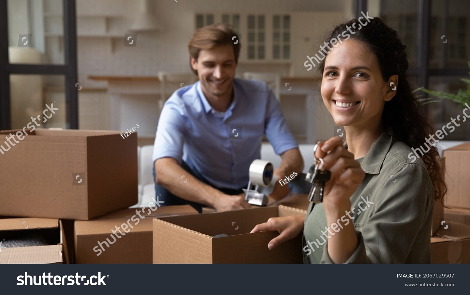 Happy young couple pack their belongings move out of rented house to their own, Hispanic wife smile look at camera hold bunch of keys symbol of relocation, bank loan and life changes, move day concept #2067029507