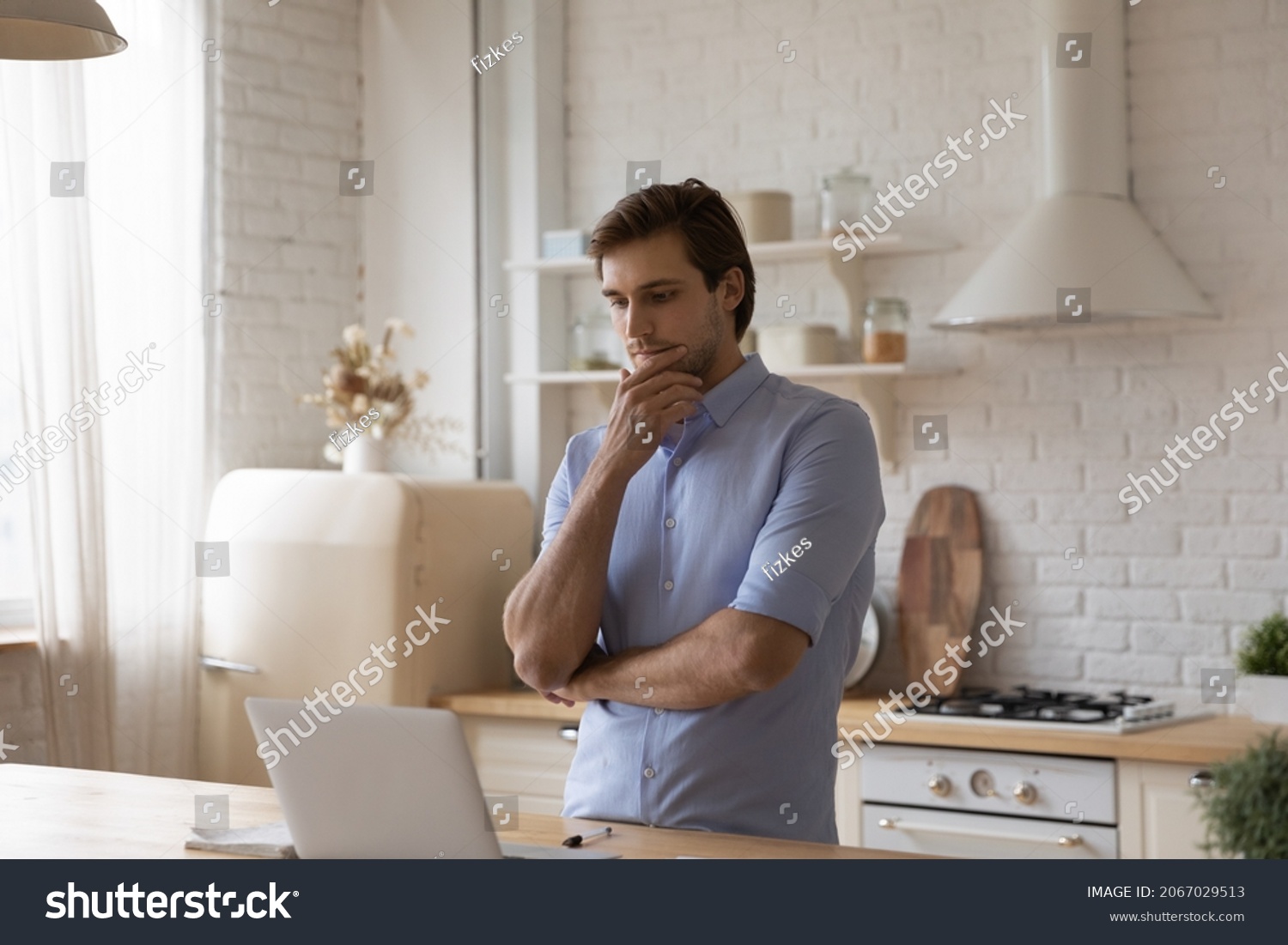 Pensive businessman standing in kitchen staring at laptop screen thinks over task looks thoughtful, work on online project, freelancing and telecommuting occupation from home, use modern tech concept #2067029513