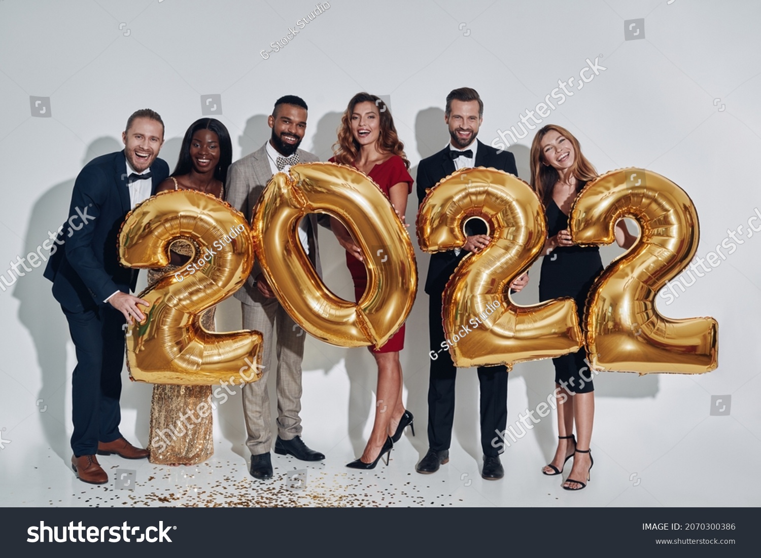 Group of beautiful people in formalwear carrying gold colored numbers and smiling #2070300386