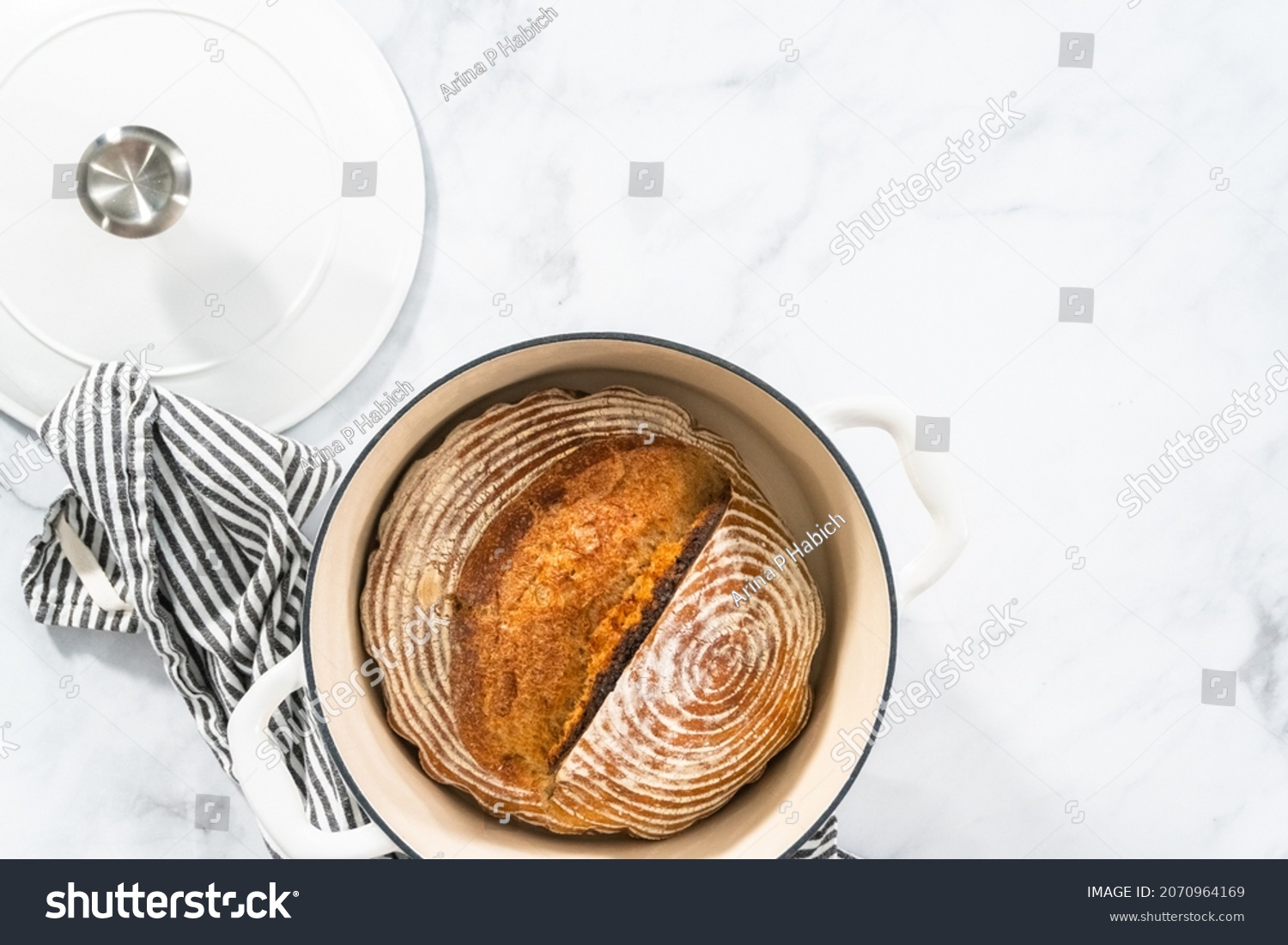 Flat lay. Freshly baked loaf of a wheat sourdough bread with marks from bread proofing basket in enameled cast iron dutch oven. #2070964169