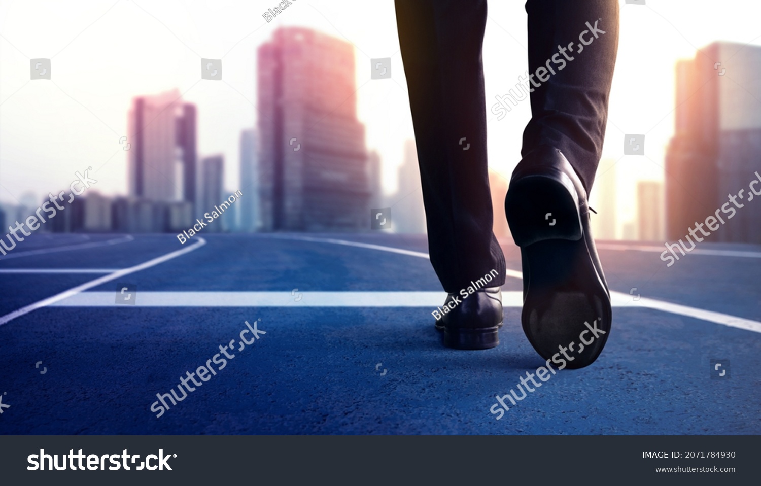 Start, Competition Concept. Low Section of Businessman Steps into Start Line on Running Track and Moving Forward to New Challenge. Blurred City Building as background #2071784930