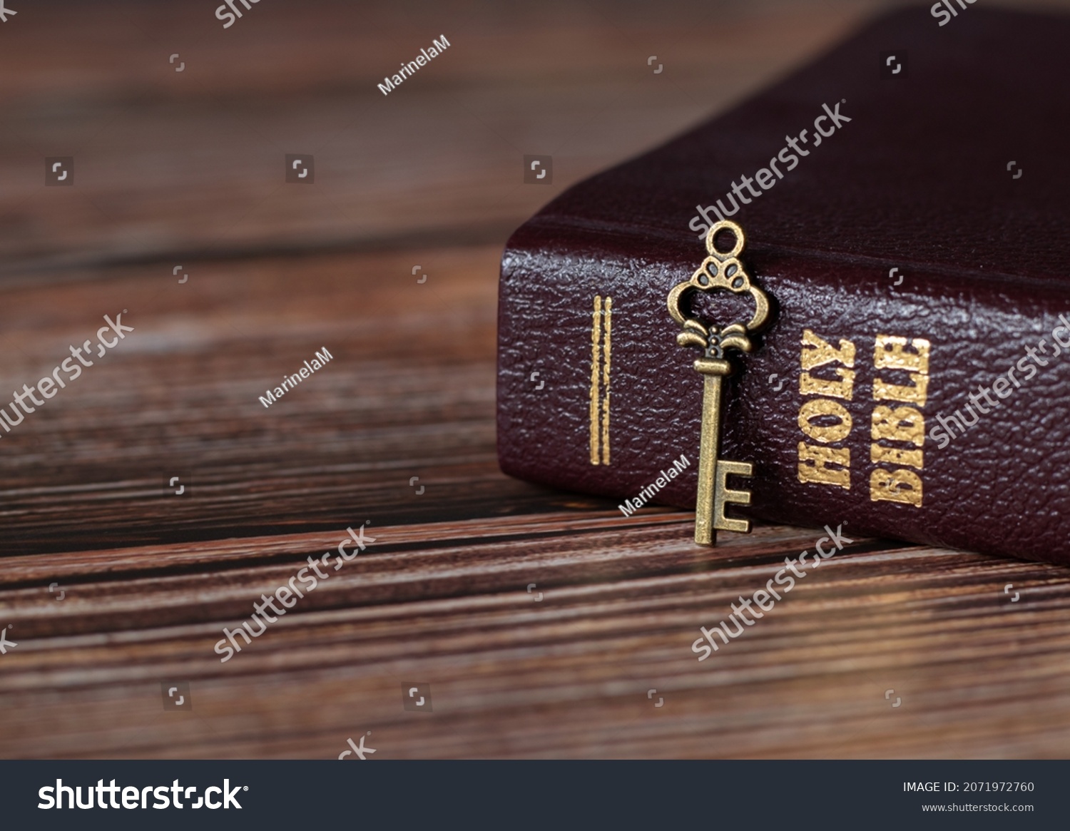 A rustic old vintage retro key with closed Holy Bible book with gold text on a wooden table. A Christian biblical concept of revelation, prayer, faith, and trust in God Jesus Christ. A close-up. #2071972760