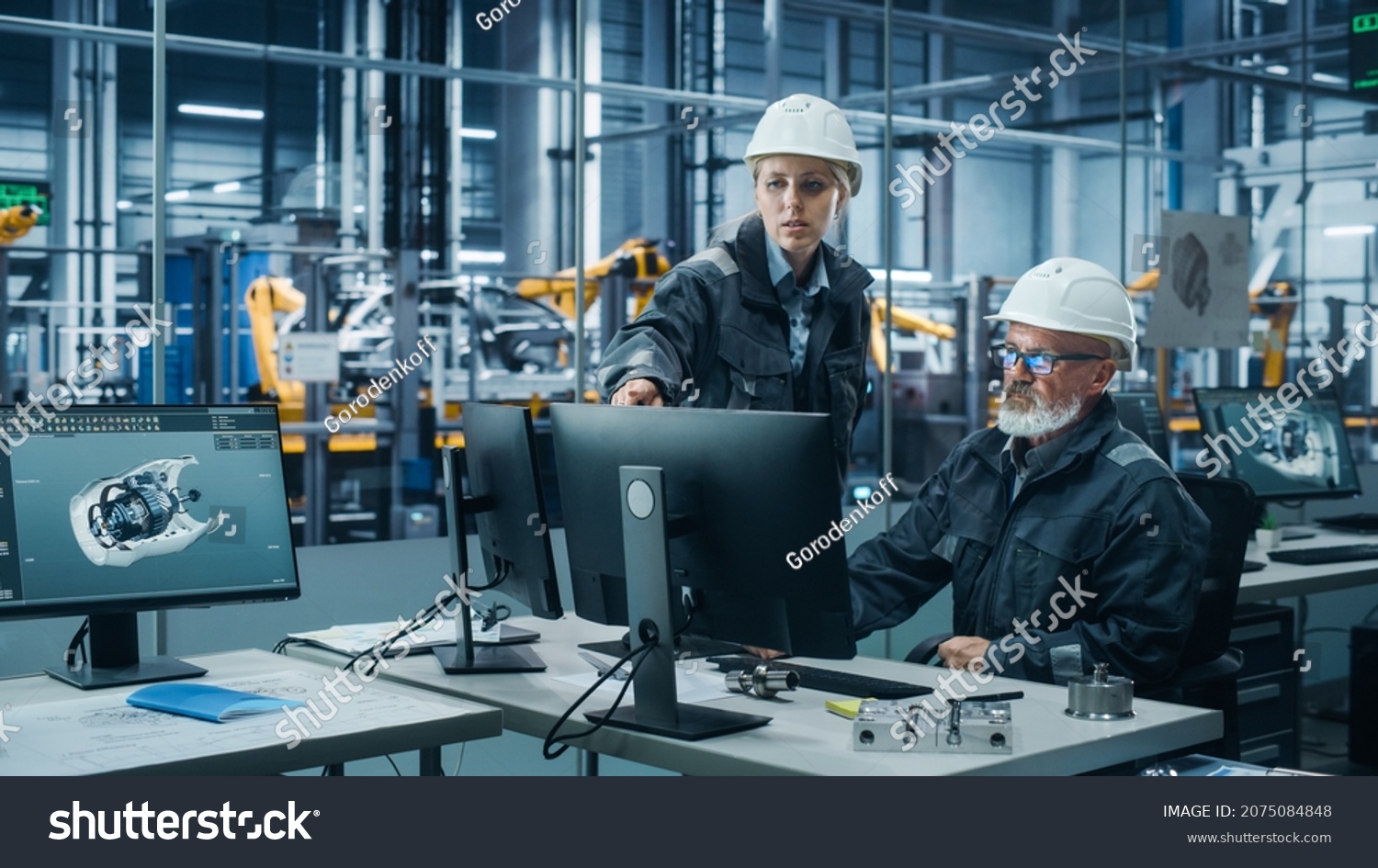 Car Factory Office: Female Manager Talks to Male Automotive Engineer Working on Computer. Automated Robot Arm Assembly Line Manufacturing Electric Vehicles. Technicians Monitoring Conveyor Production #2075084848