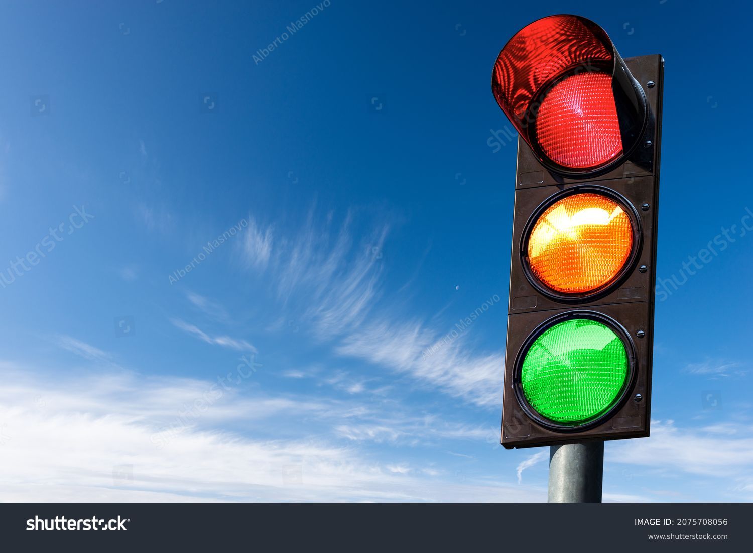Closeup of a traffic light on a blue sky with clouds and copy space, with all three lights on, green, orange and red. Italy, Europe. #2075708056