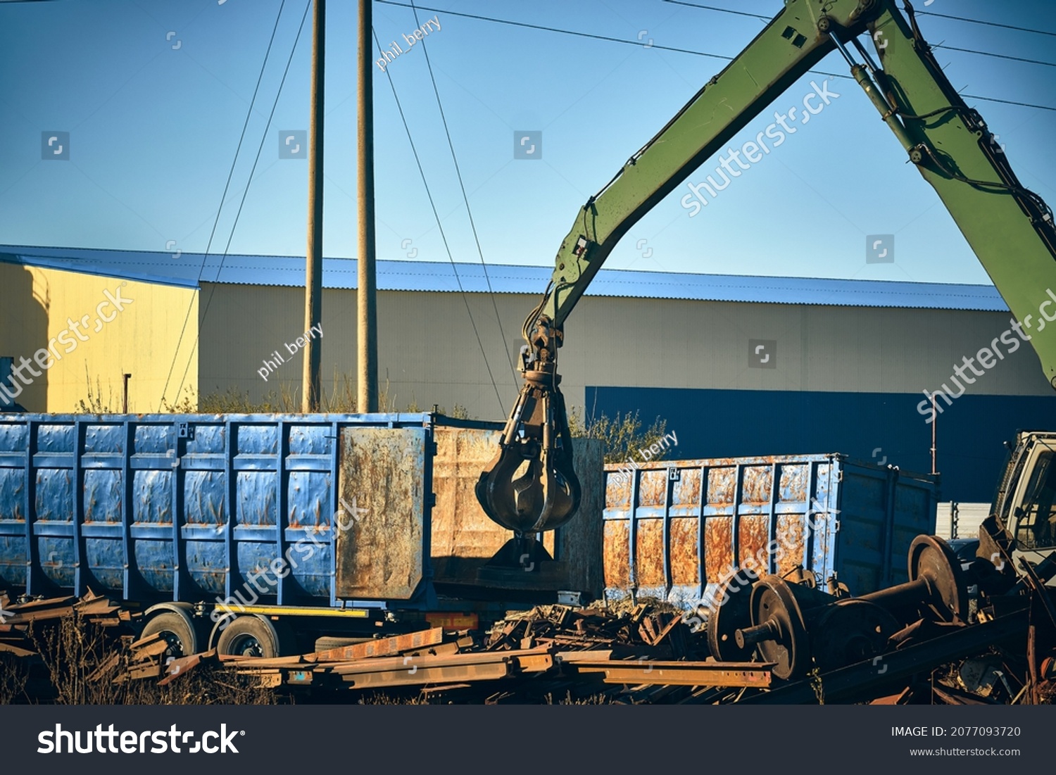 Grapper loader loads truck with scrap metal. Hand of grabber excavator loading recycle metal waste to truck. Clamshell at scrap metal yard #2077093720