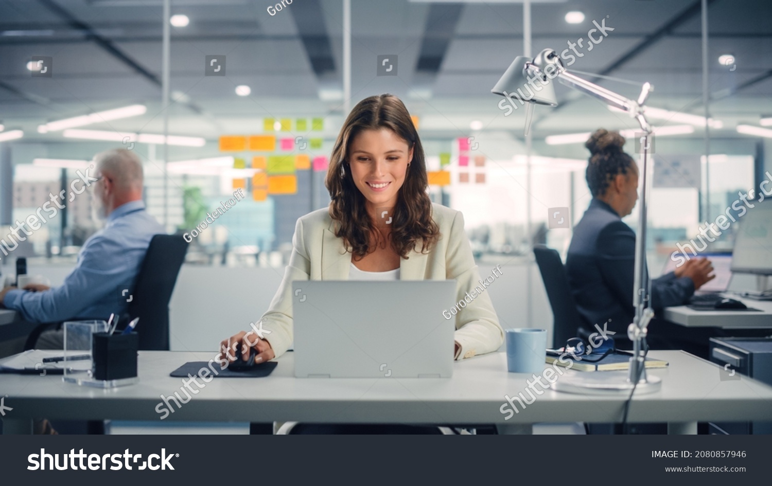 Young Happy Businesswoman Using Computer in Modern Office with Colleagues. Stylish Beautiful Manager Smiling, Working on Financial and Marketing Projects. Drinking Tea or Coffee from a Mug. #2080857946