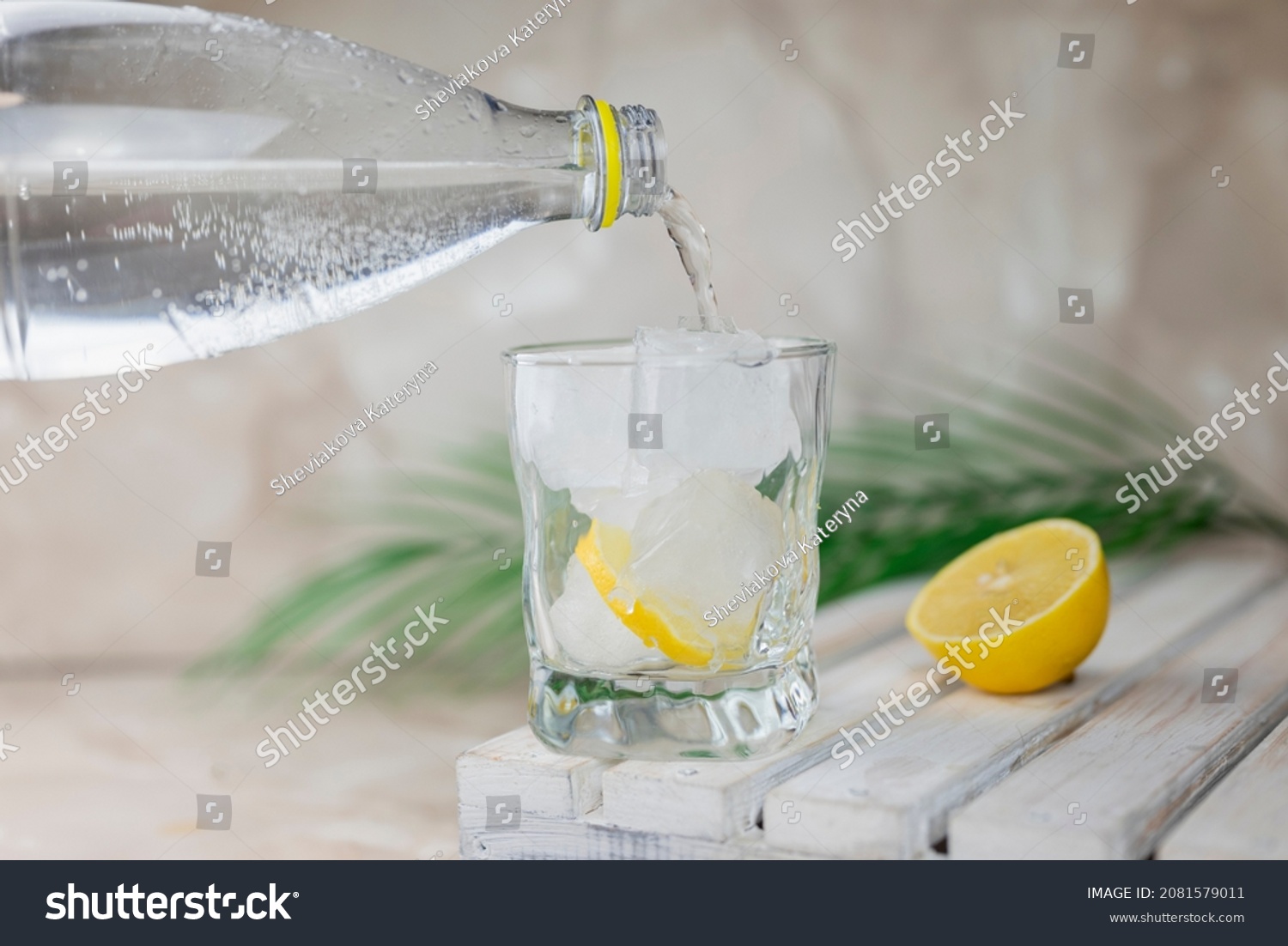 water or tonic is poured from a bottle into a glass with ice and lemon #2081579011