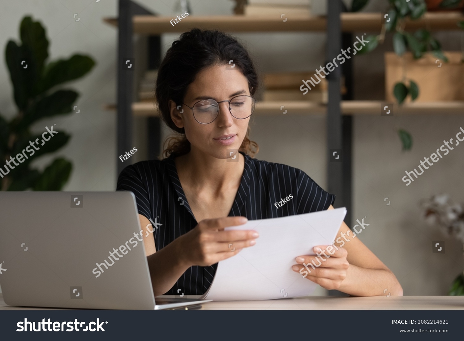 Important papers. Serious hispanic female manager in glasses engaged in office paperwork study project documentation cover letter. Young woman hr reading resume thinking on applicant cv at workplace #2082214621