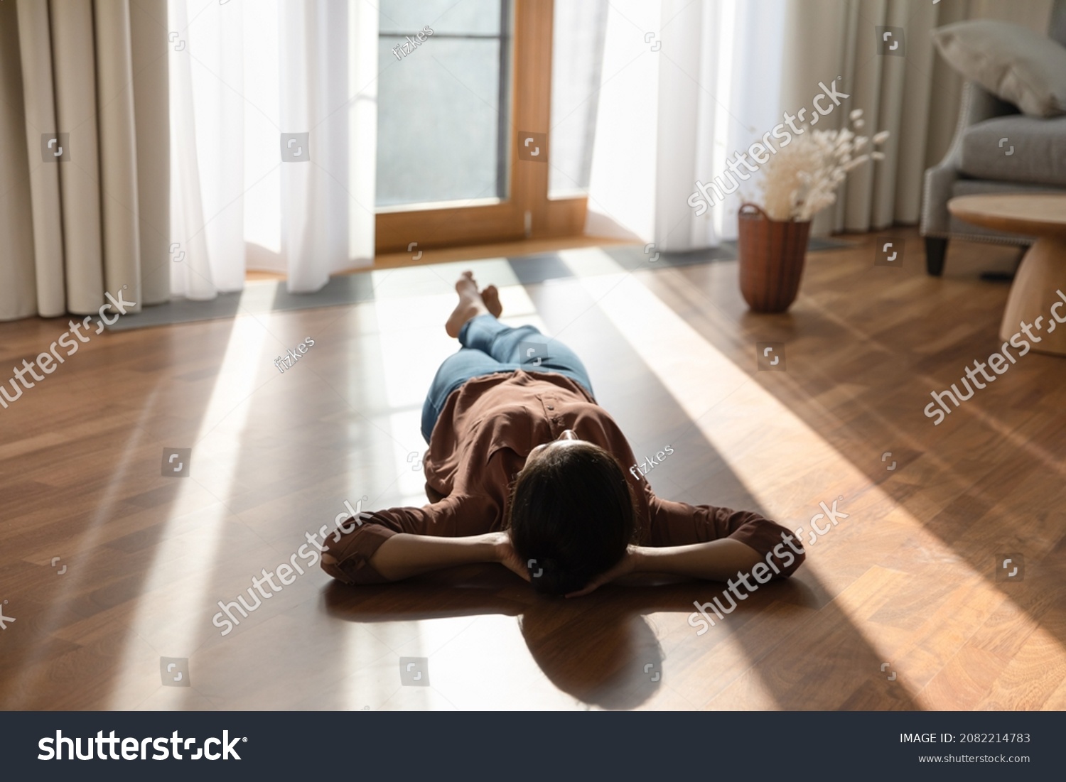 Relaxed happy young indian ethnicity woman homeowner lying alone on warm wooden floor with underfloor heating, enjoying carefree peaceful weekend leisure time alone in modern stylish living room. #2082214783