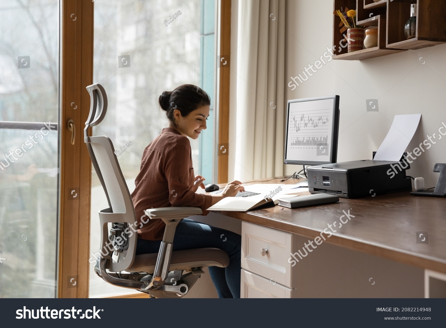 Concentrated young indian ethnicity woman sitting in comfortable adjustable ergonomic armchair with lumbar support, studying or working on computer in modern home office. distant workday concept. #2082214948