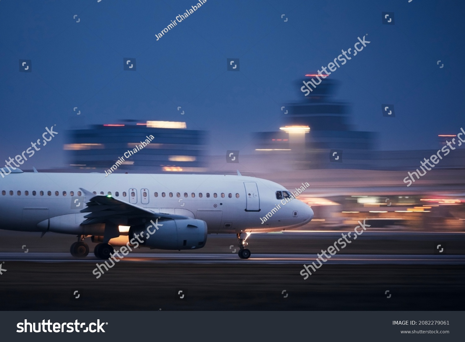 Airplane during take off on airport runway at night against air traffic control tower. Plane in blurred motion at night. #2082279061
