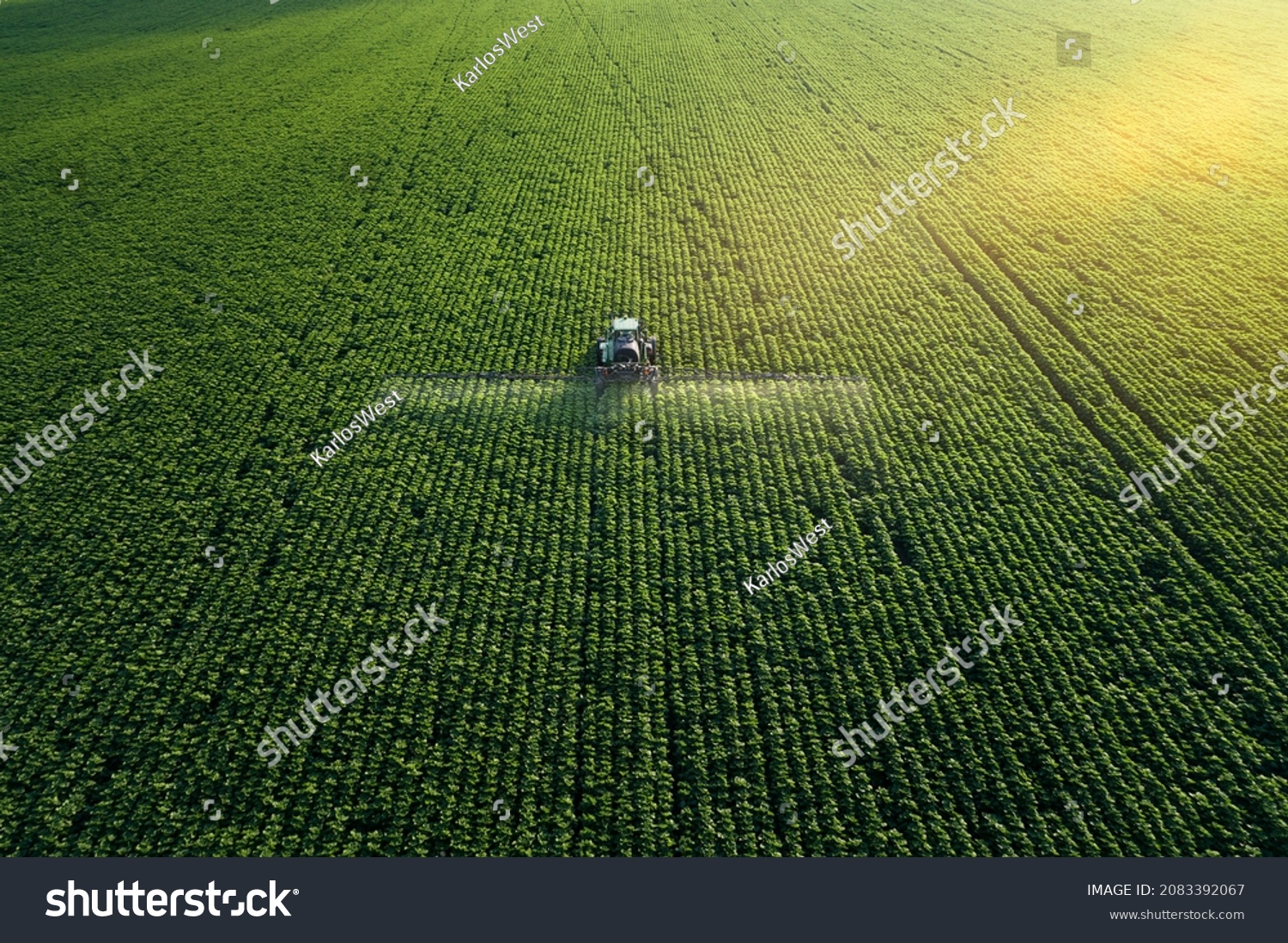 Taking care of the Crop. Aerial view of a Tractor fertilizing a cultivated agricultural field. #2083392067