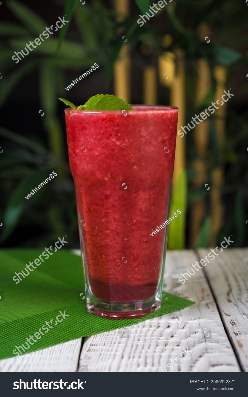 The photo of a strawberry smoothie. The glass is placed on the wooden bar. The forest and a lake are in the background #2086922872