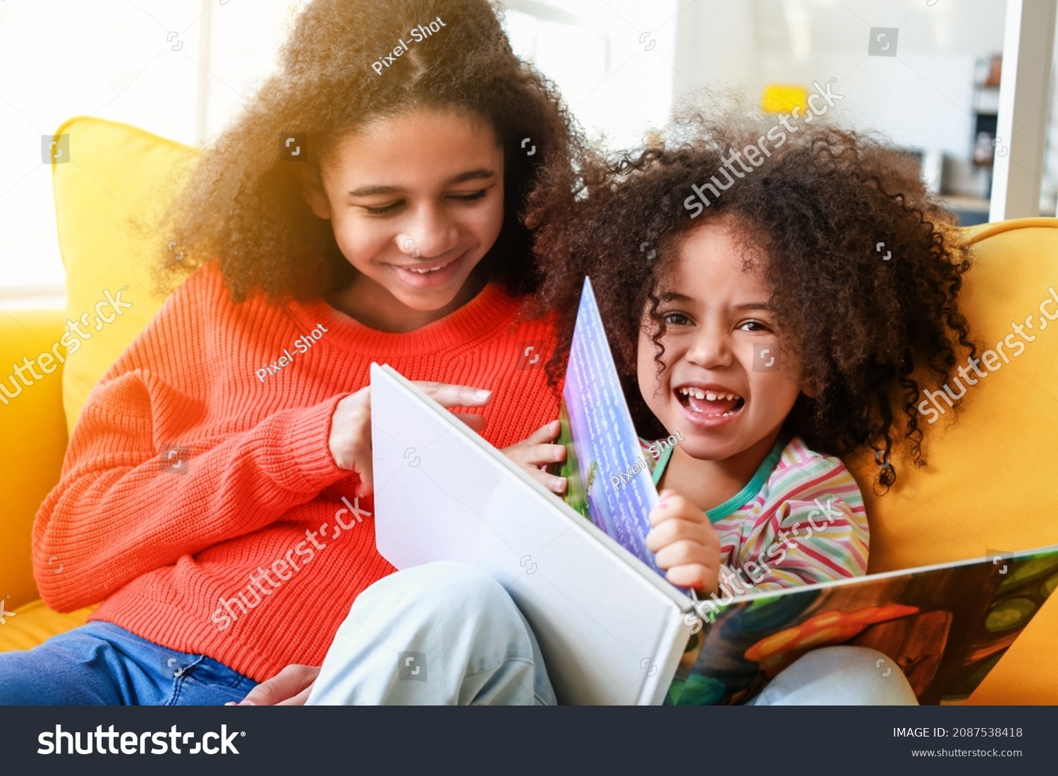 Cute African-American sisters reading book at home #2087538418
