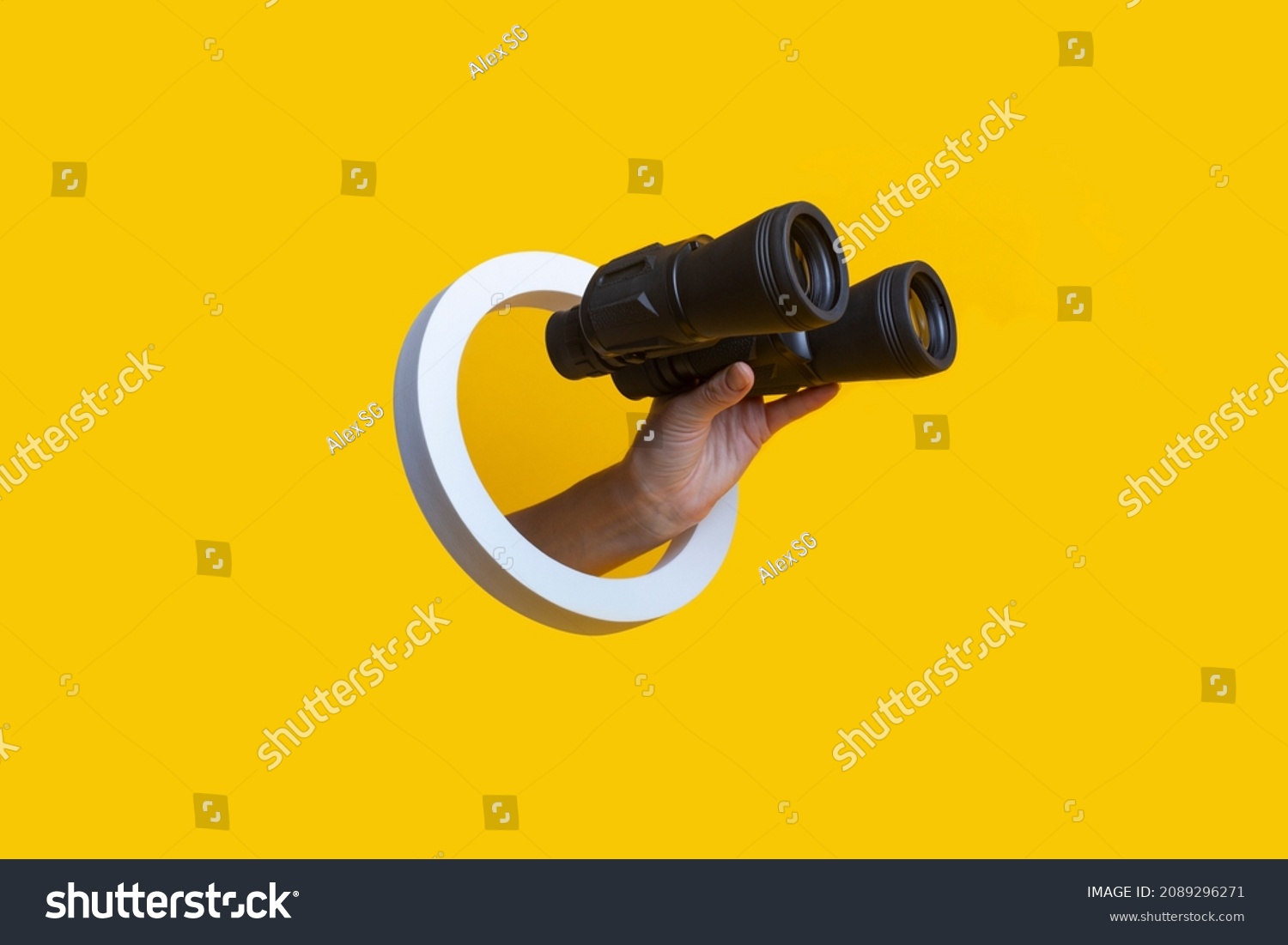 Woman's hand holding binoculars in a hole on a yellow background  #2089296271