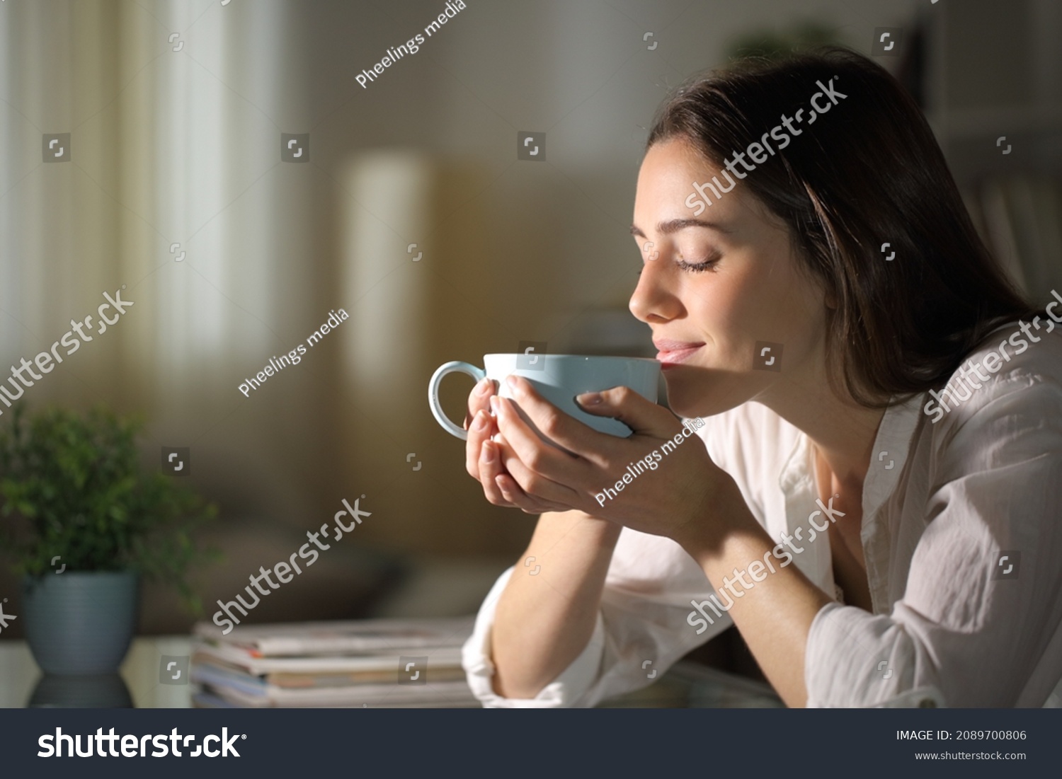 Relaxed woman smelling coffee in the morning sitting in the living room at home #2089700806