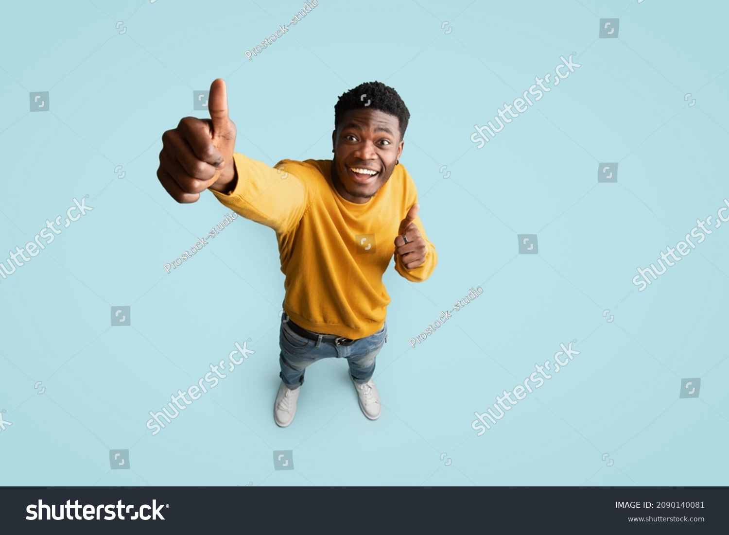 Top view of joyful handsome african american millennial guy in nice outfit showing thumb up and smiling at camera on blue studio background, recommending something exciting, copy space, full length #2090140081