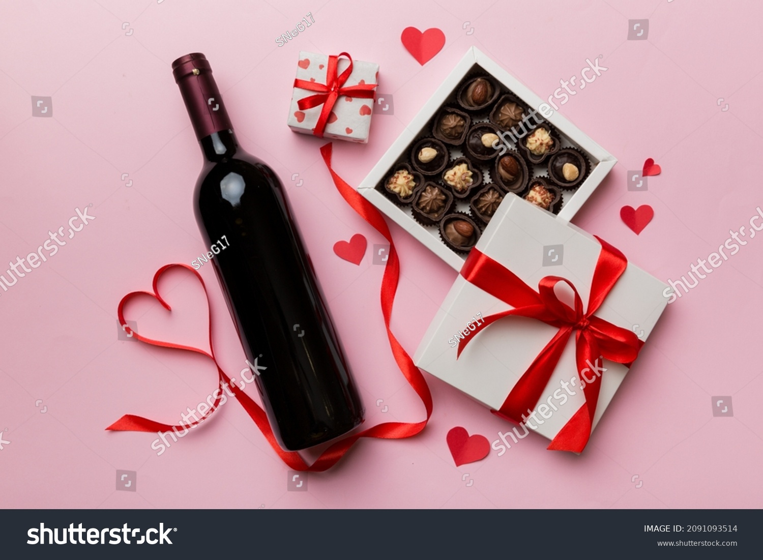Bottle of red wine on colored background for Valentine Day with gift and chocolate. Heart shaped with gift box of chocolates top view with copy space. #2091093514