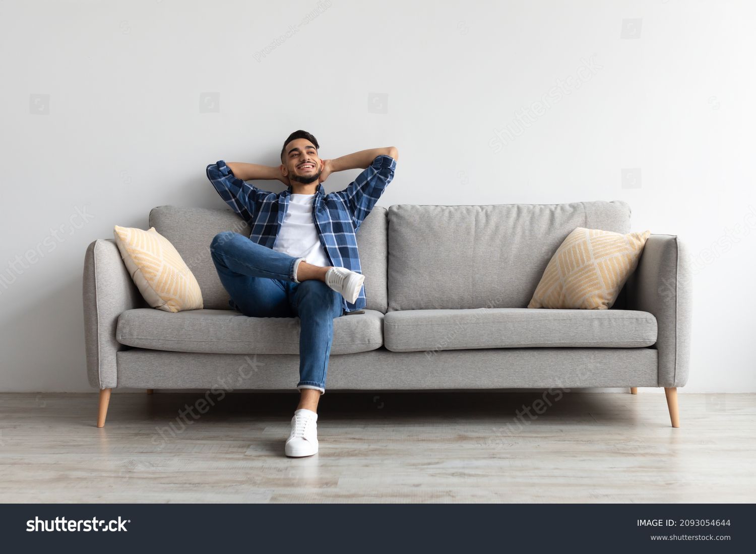 Rest Concept. Happy Middle Eastern guy sitting on comfortable couch at home in living room. Cheerful casual man relaxing on sofa, leaning back, enjoying weekend free time or break from work #2093054644