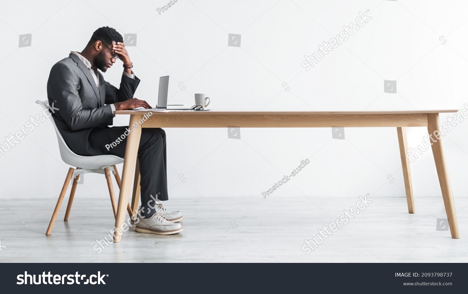 Side view of young black office employee feeling tired of working overtime, sitting at desk with laptop against white studio wall, copy space. Exhausted businessman having problem with online job #2093798737