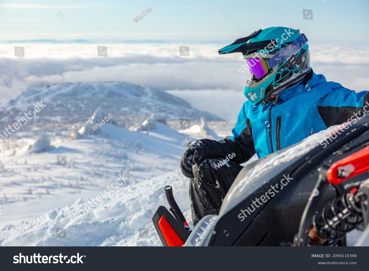 a snowmobiler is resting on top of a mountain, tipping the snowmobile on its side. snowmobile close-up with a sitting rider over the valley #2094110398