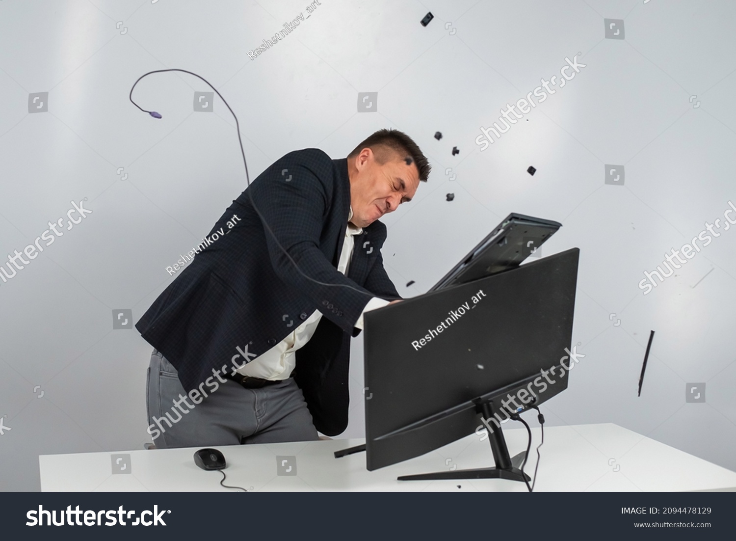 Caucasian man in a suit gets angry and smashes the keyboard on the monitor. An office worker in a rage breaks the computer. #2094478129