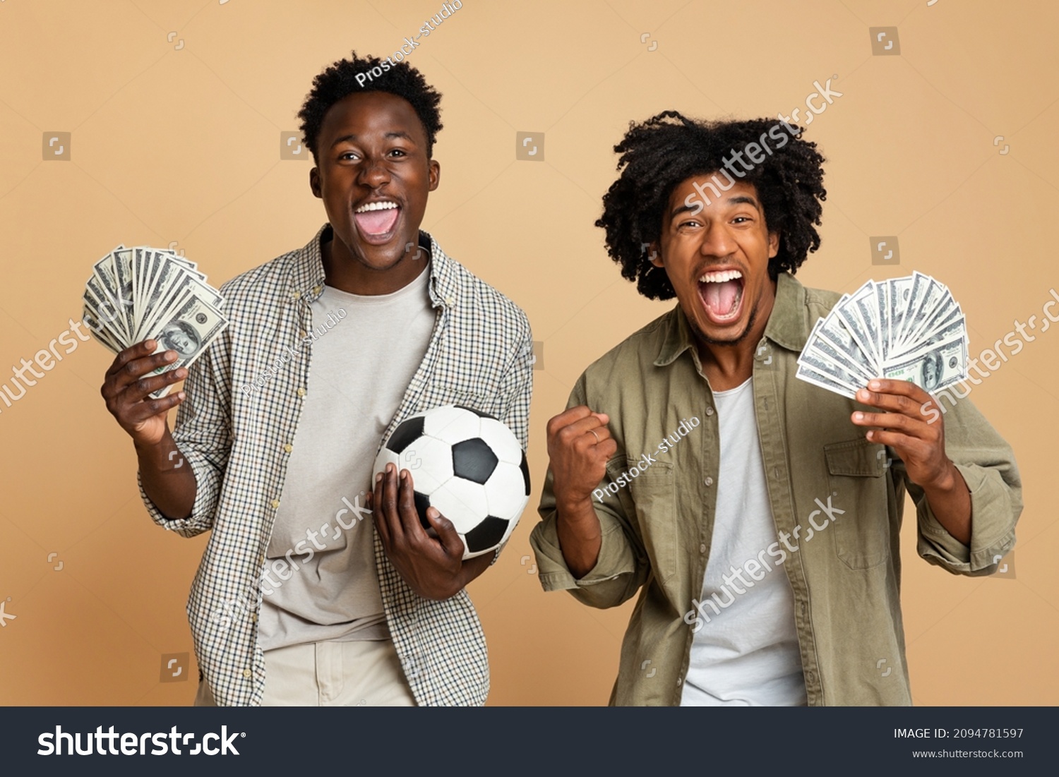 Sport Bets. Portrait Of Excited Black Guys With Football Ball And Money Standing Over Beige Background, Cheerful Soccer Fans Celebrating Success With Dollar Cash, Emotionally Reacting To Win #2094781597