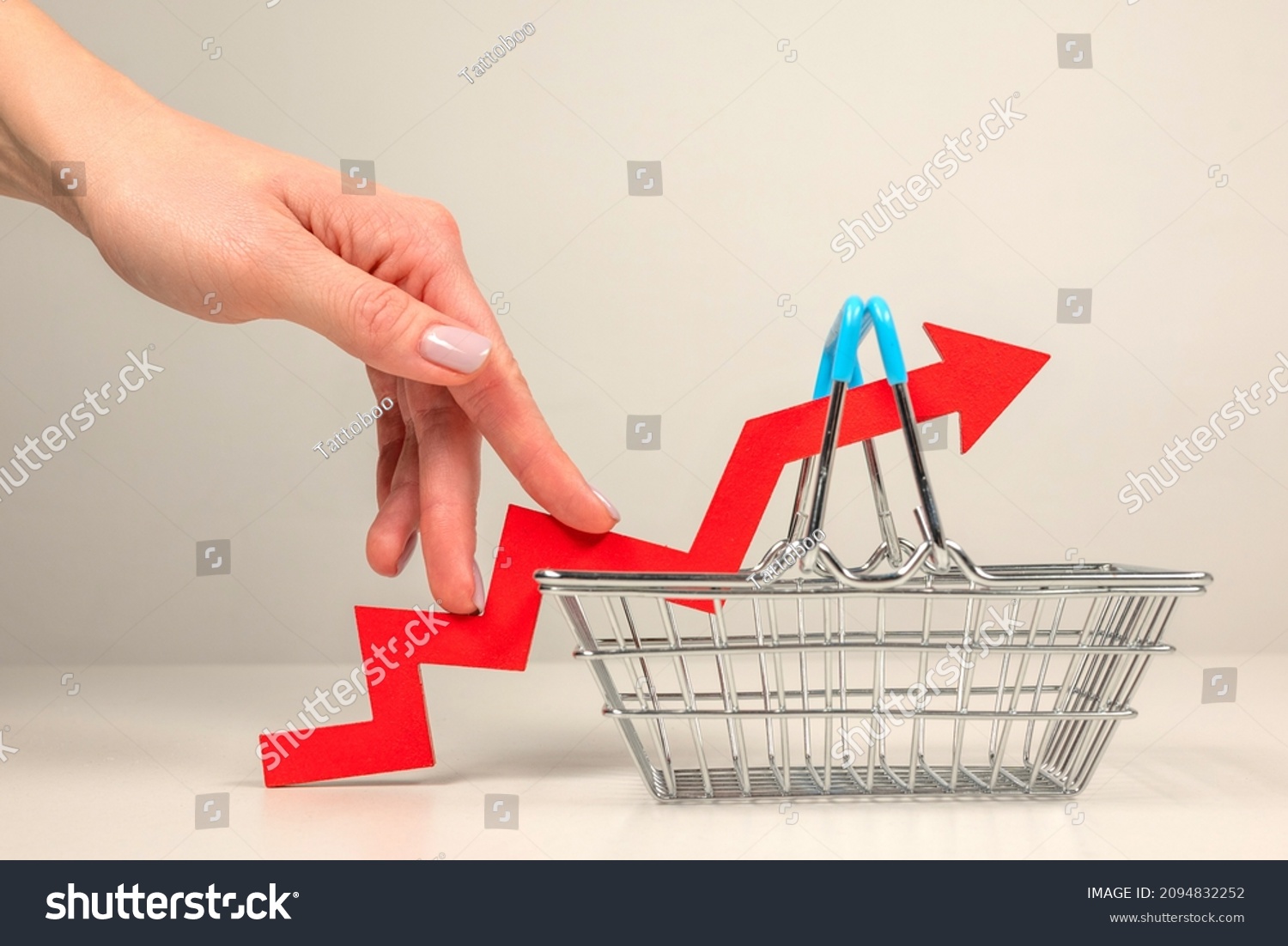 The fingers of a woman's hand step up the arrow of a chart lying on a shopping basket. Crisis and rising commodity prices concept #2094832252