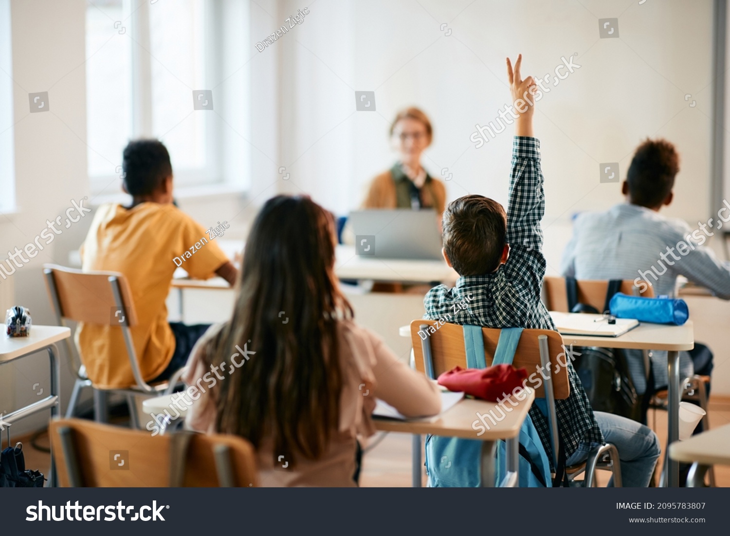 Rear view of schoolboy raising his arm to ask a question during a class in the classroom. #2095783807