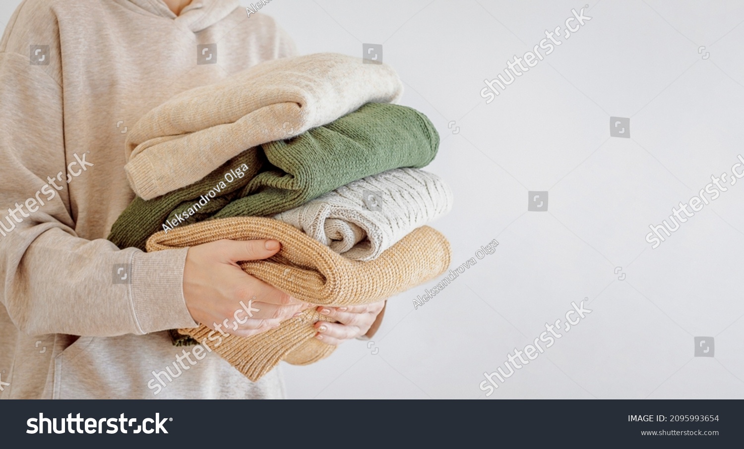 Woman's hand holding a stack of clothes. Clothes Donation, Renewable Concept.Preparing Garment at Home before Donate. Woman packs clothes for a donation or for moving #2095993654