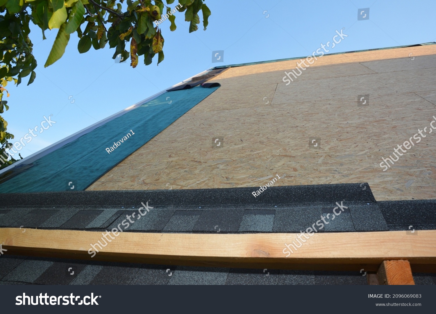 New roofing construction and asphalt shingles installation. A close-up of asphalt shingles installation on plywood, osb roof sheathing and waterproofing roof underlayment. #2096069083