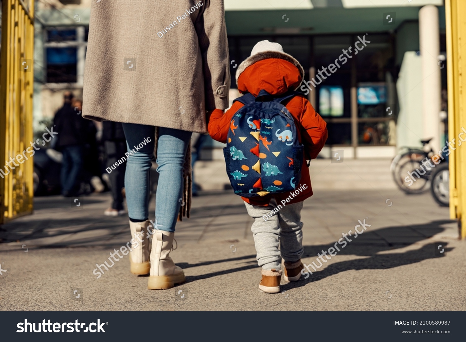 A mother entering the kindergarten yard with her preschooler boy. #2100589987