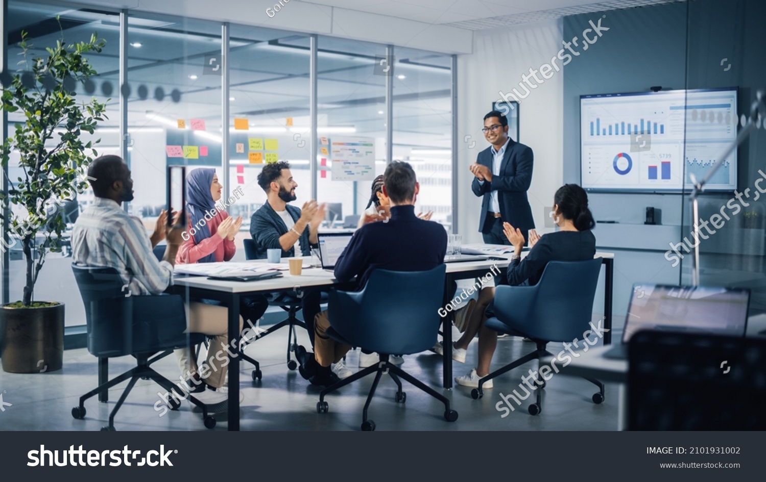 Multi-Ethnic Office Conference Room. Indian CEO does Presentation for Diverse Young Entrepreneurs, Talking, Using TV with Infographics, Statistics, Graphs. Businesspeople Invest in e-Commerce Startup #2101931002