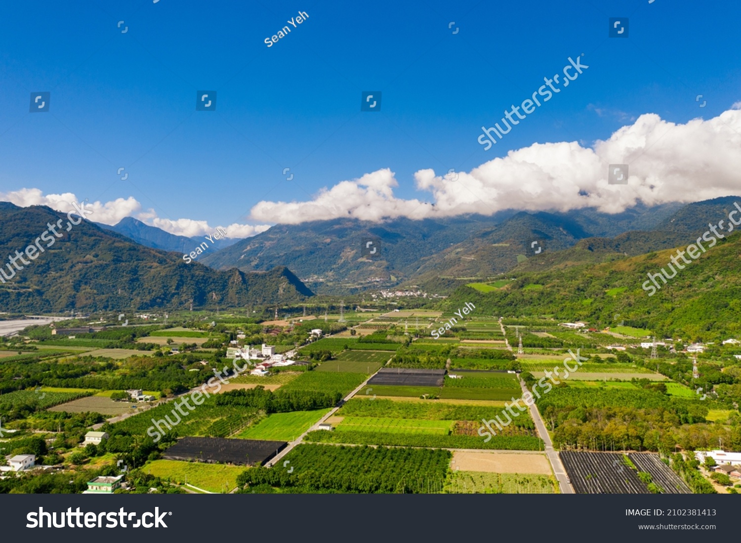 Aerial of square, green green paddy, trees and mountain with blue sky and cloud under sunny day in Longtian Village, Luye township, Taitung. A famous country with Checkerboard street, Japanese shrine. #2102381413