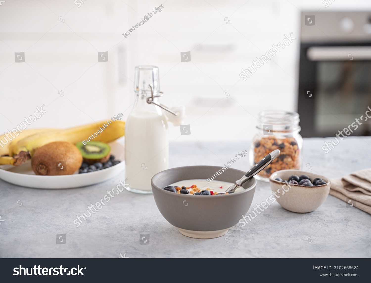 The concept of a healthy breakfast of vegetarian yogurt, granola and fresh fruit on a blue table against a white  kitchen background. Front view. #2102668624