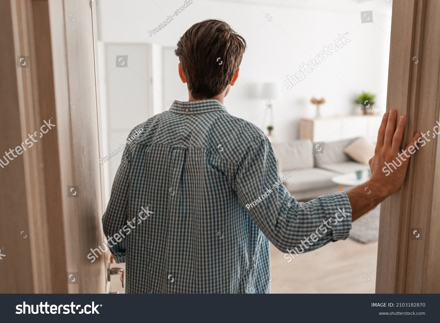 Back rear view of unrecognizable young man walking in his apartment, entering new home, casual guy standing in doorway of modern flat, looking at design interior, coming inside, selective focus #2103182870