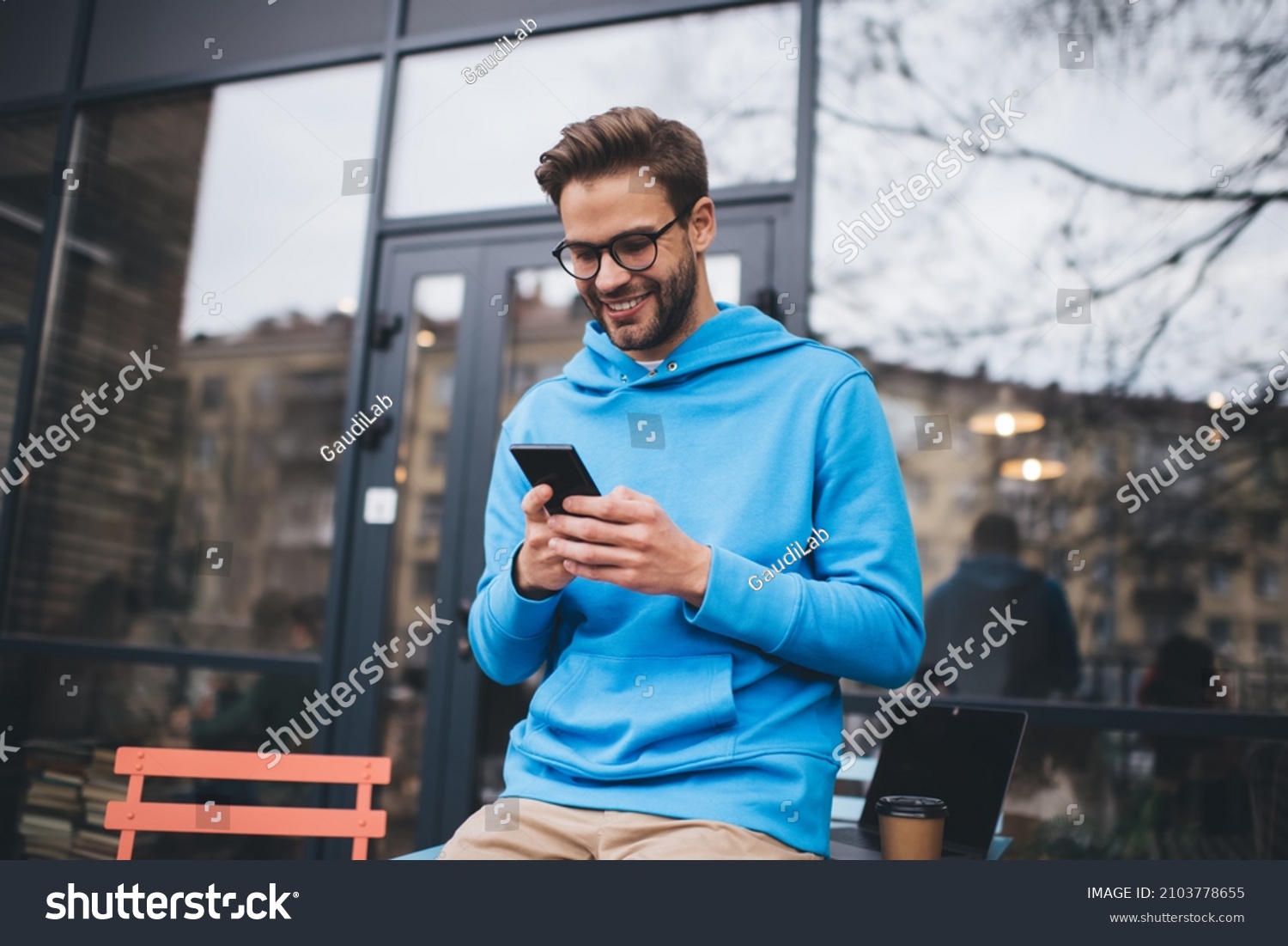 Happy hipster guy in classic spectacles for provide vision correction using cellphone gadget for checking received email message, smiling Caucasian male blogger browsing website in social media #2103778655