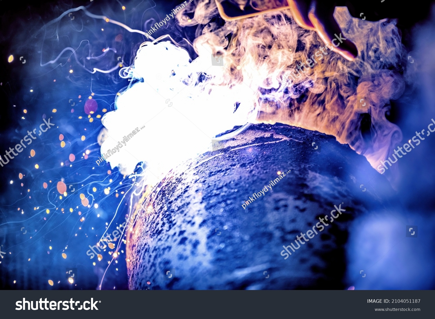 A welder welds metal into his workshop. Blue welding sparks. Gas combustion and blue smoke. Small welding workshop. Welding juncture of metal construction #2104051187