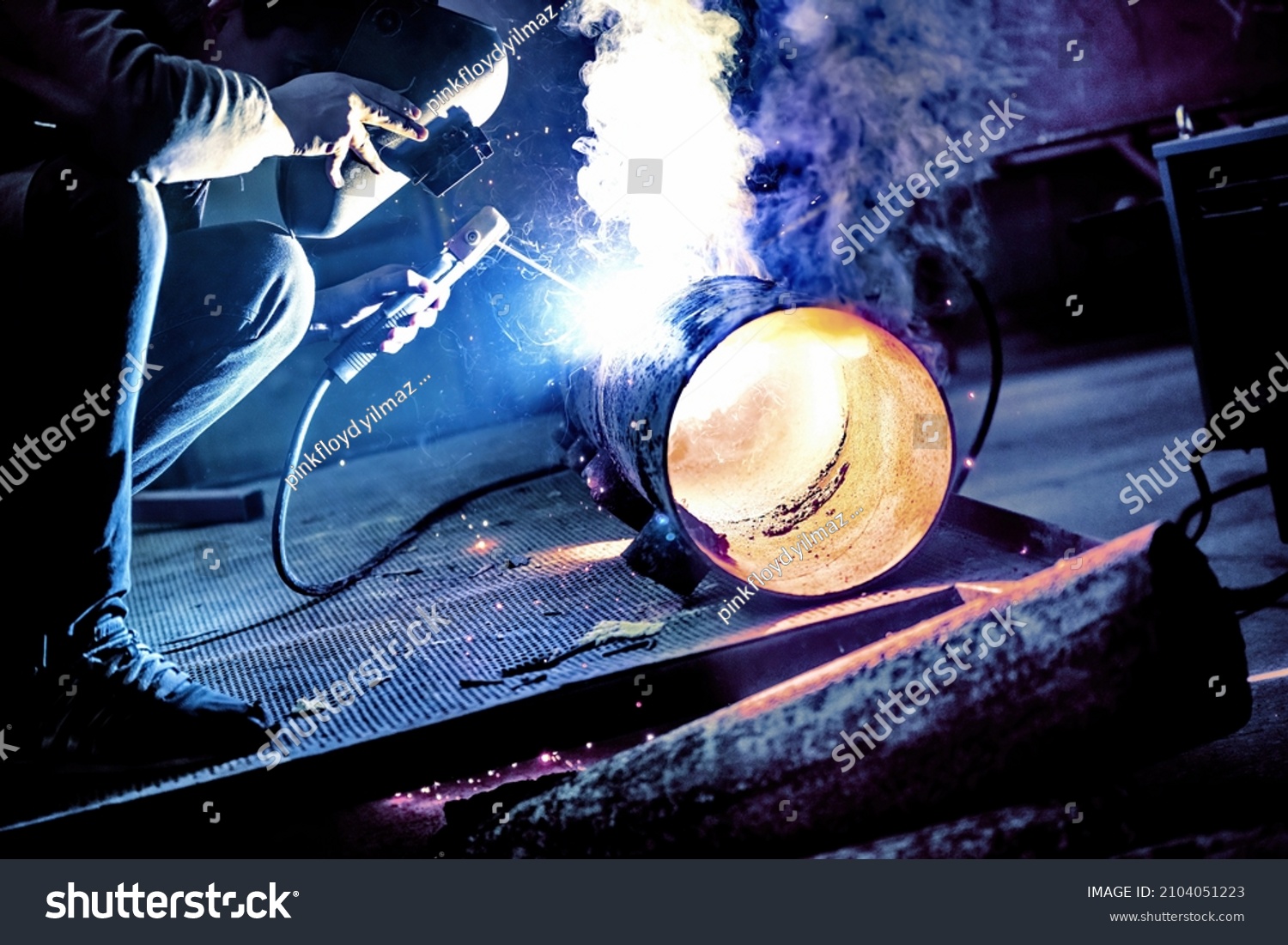 A welder welds metal into his workshop. Blue welding sparks. Gas combustion and blue smoke. Small welding workshop. Welding juncture of metal construction #2104051223