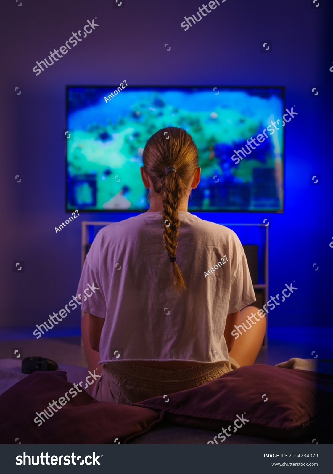 A blonde girl is sitting on the sofa and watching TV. Blue neon light. Watching your favorite films and TV shows, rest, relaxation, insomnia, loneliness, quarantine, self-isolation. #2104234079