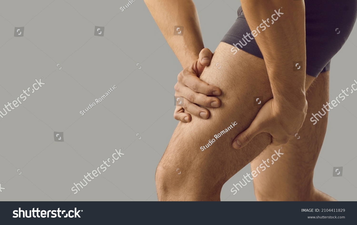 Man feeling pain or having thigh cramp. Sportsman who's suffering from hamstring muscles pain after running, jogging or gym fitness training standing on grey copy space background and touching his leg #2104411829